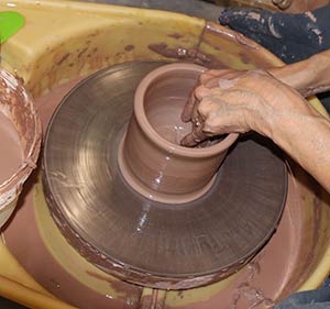 a photo of a potter forming a piece of pottery at a potters wheel