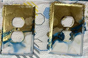 a light switch with gold and turquoise colors painted on it with alcohol ink