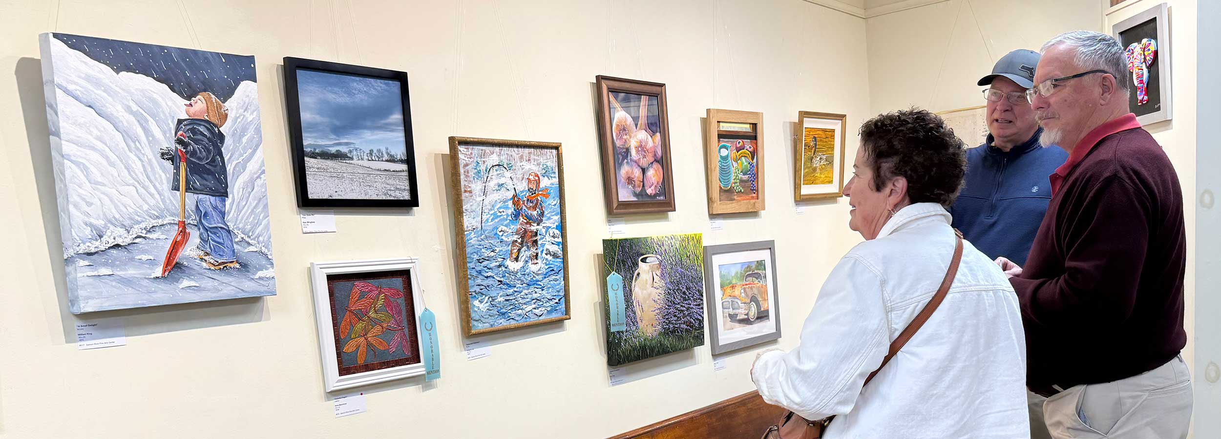 a banner photo showing three people looking at various pieces of artwork from the Sunday Artist Show 2025