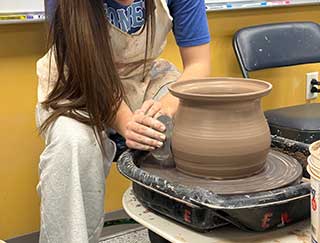 an image of a young adult shaping a vessel on a pottery wheel
